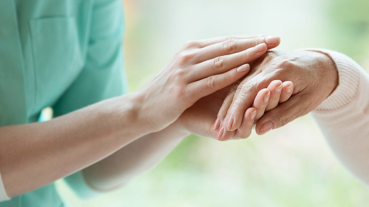 Νοσοκόμα κρατά τα χέρια ασθενούς με Πάρκινσον