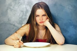 πεινασμένη κοπέλα κάθεται μπροστά σε ένα άδειο πιάτο