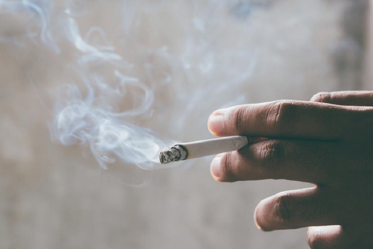 χέρι άνδρα κρατά ένα αναμμένο τσιγάρο και απολαμβάνει το κάπνισμα