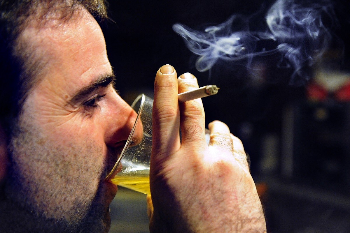 άνδρας πίνει αλκοόλ και κρατά στο χέρι του ένα αναμένο τσιγάρο