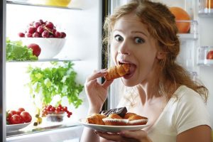 νεαρή γυναίκα τρώει φαγητό μέσα από το ψυγείο
