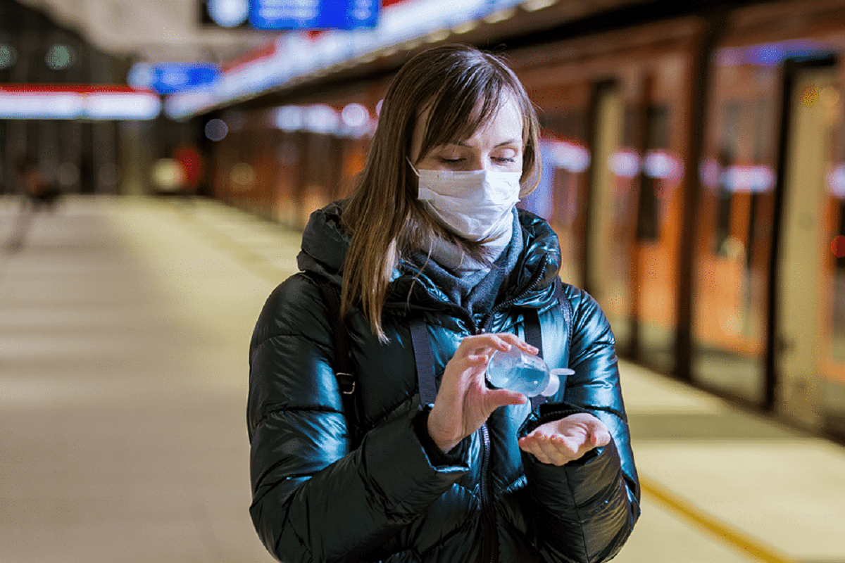 νεαρή γυναίκα φοράει μάσκα και βάζει αντισυπτικό για να μην διαδοθεί ο κορωνοϊός