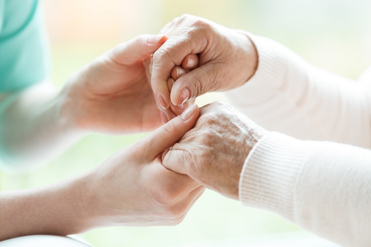 νεαρή γυναίκα κρατά τα χέρια ηλικιωμένης με Αλτσχάιμερ