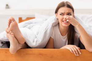γυναίκα κρατά την μύτη της γιατί τα πόδια δίπλα της μυρίζουν άσχημα